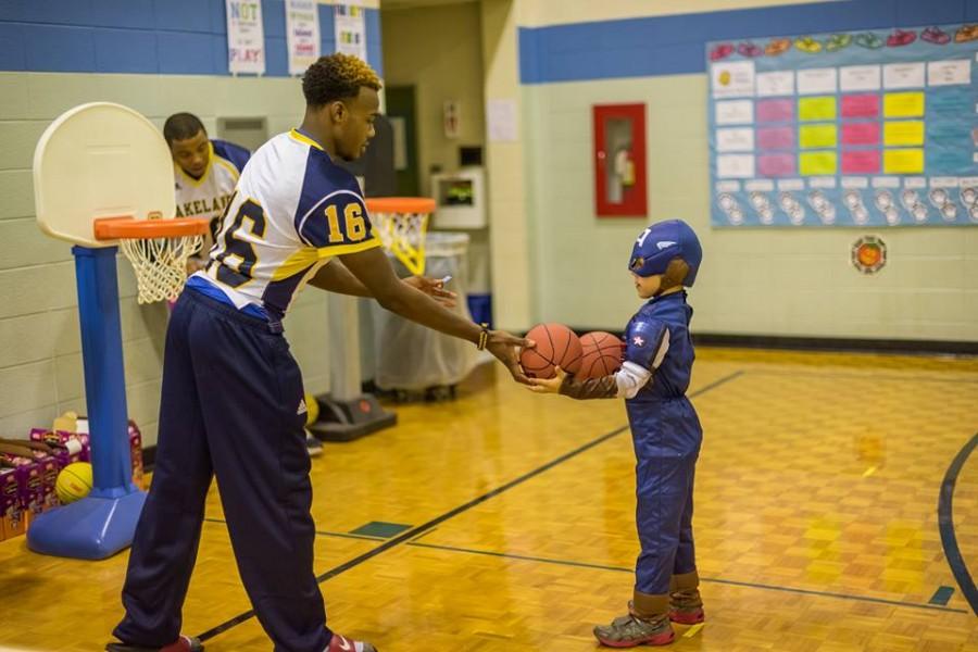 Sophomore Donte Rowell helps a little Captain America shoot hoops at Lincoln-Erdman Elementary Schools Halloween event.