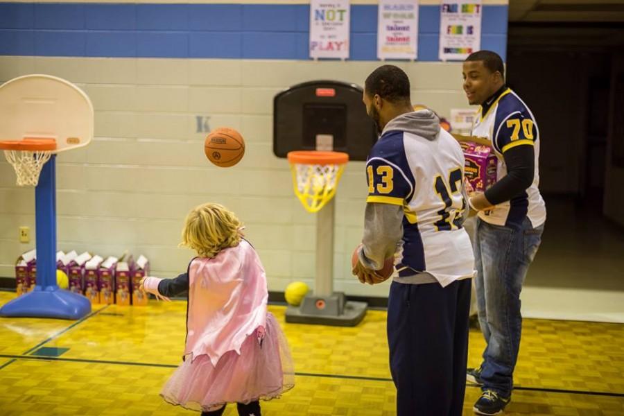 Sophomore Jawon Turner (center) and senior Vincent Stepney-Willis (right) cheer on a young superhero at Lincoln-Erdman Elementary Schools Halloween event.