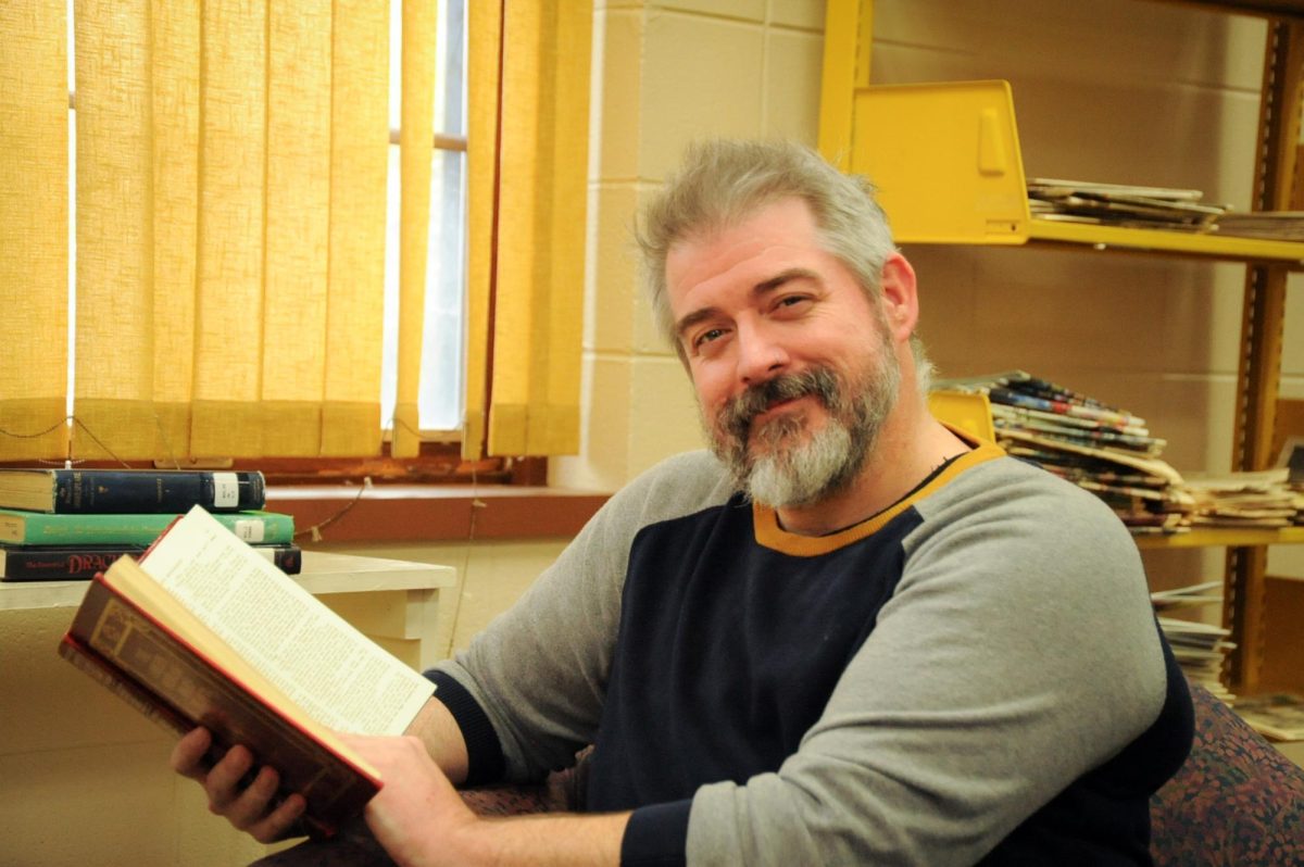 A professor holding a book smiles at the camera.