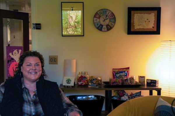 A seated woman smiles in front of a shelf with jars and bags of colorful candy.
