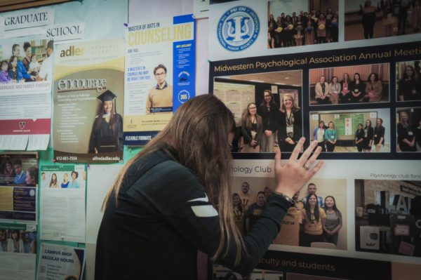 A student leans on and sadly gestures to a bulletin board of posters.