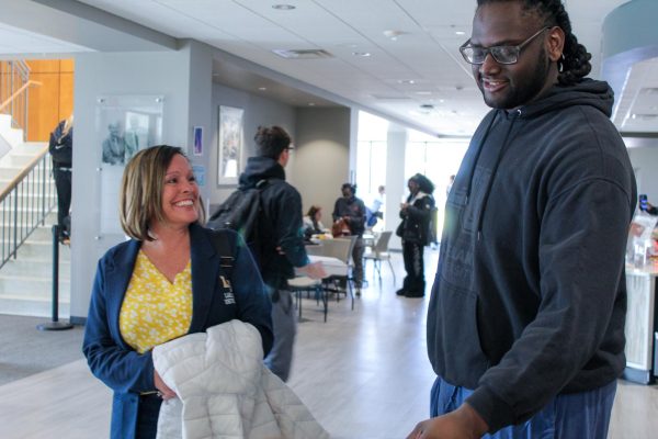 Two people smile and talk in a college building.
