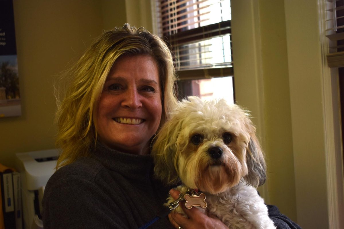 A smiling woman holds a small white dog with curly fur.