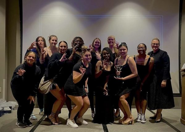 A group of college students wearing black, holding a glass trophy on a stage.